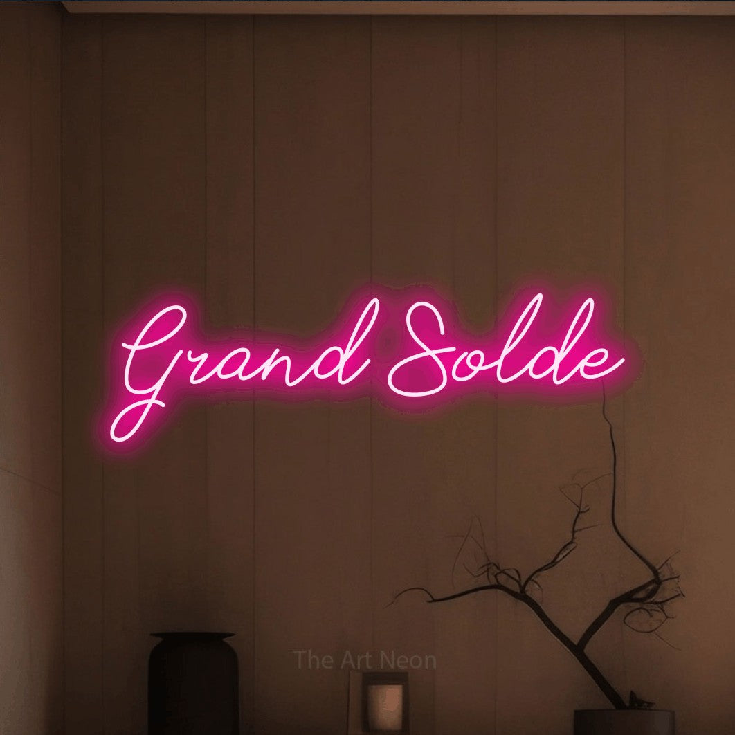 “Grand solde” LED neon sign in hot pink, with cursive lettering, shown against a simple earth-toned interior.