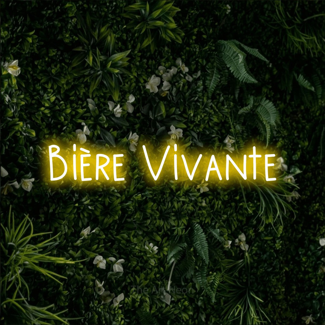 “Bière vivante” LED neon sign in yellow, with narrow hand-drawn lettering, shown against a dense green plant wall.