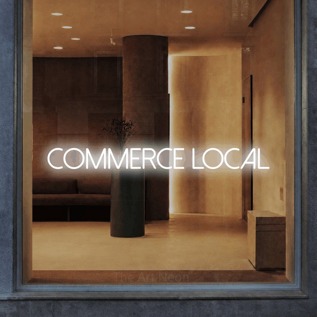 “Commerce local” LED neon sign in cool white, with thin sans-serif lettering, shown against a warm-toned interior.