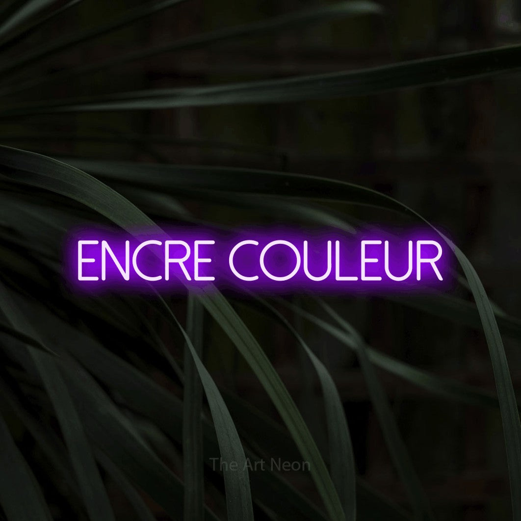“Encre couleur” LED neon sign in purple, with thin sans-serif lettering, shown against a close-up of dark foliage.