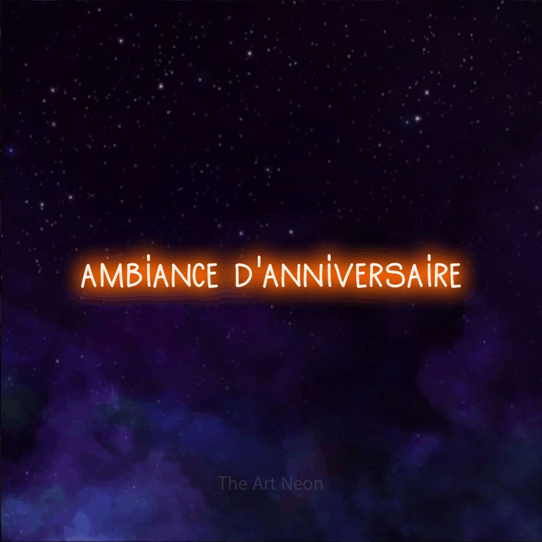 “Ambiance d'anniversaire” LED neon sign in orange, with narrow hand-drawn lettering, shown against a purple galaxy backdrop.