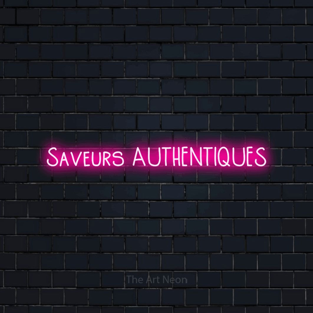 “Saveurs authentiques” LED neon sign in hot pink, with narrow hand-drawn lettering, shown against a dark navy brick wall.
