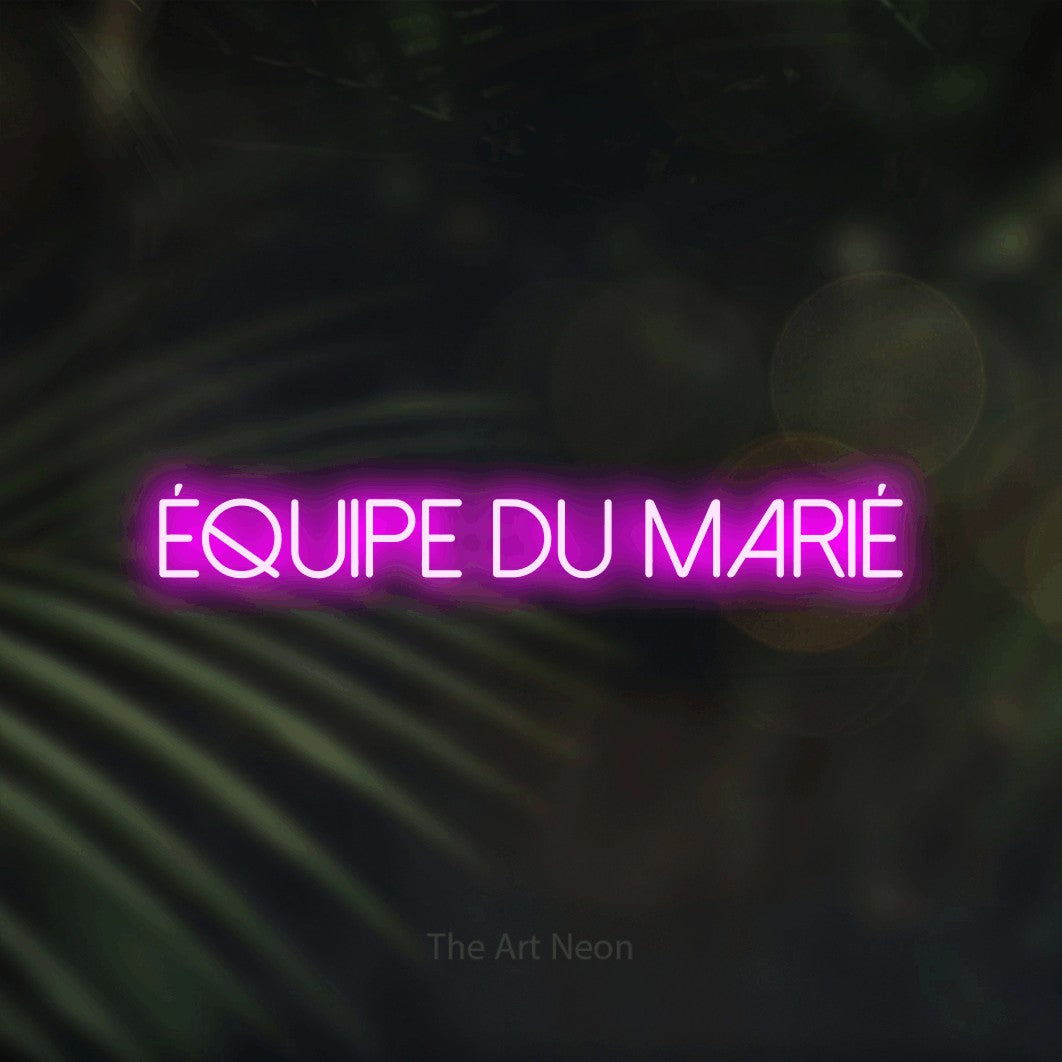 “Équipe du marié” LED neon sign in pink, with thin sans-serif lettering, shown against a blurred palm and bokeh-light backdrop.