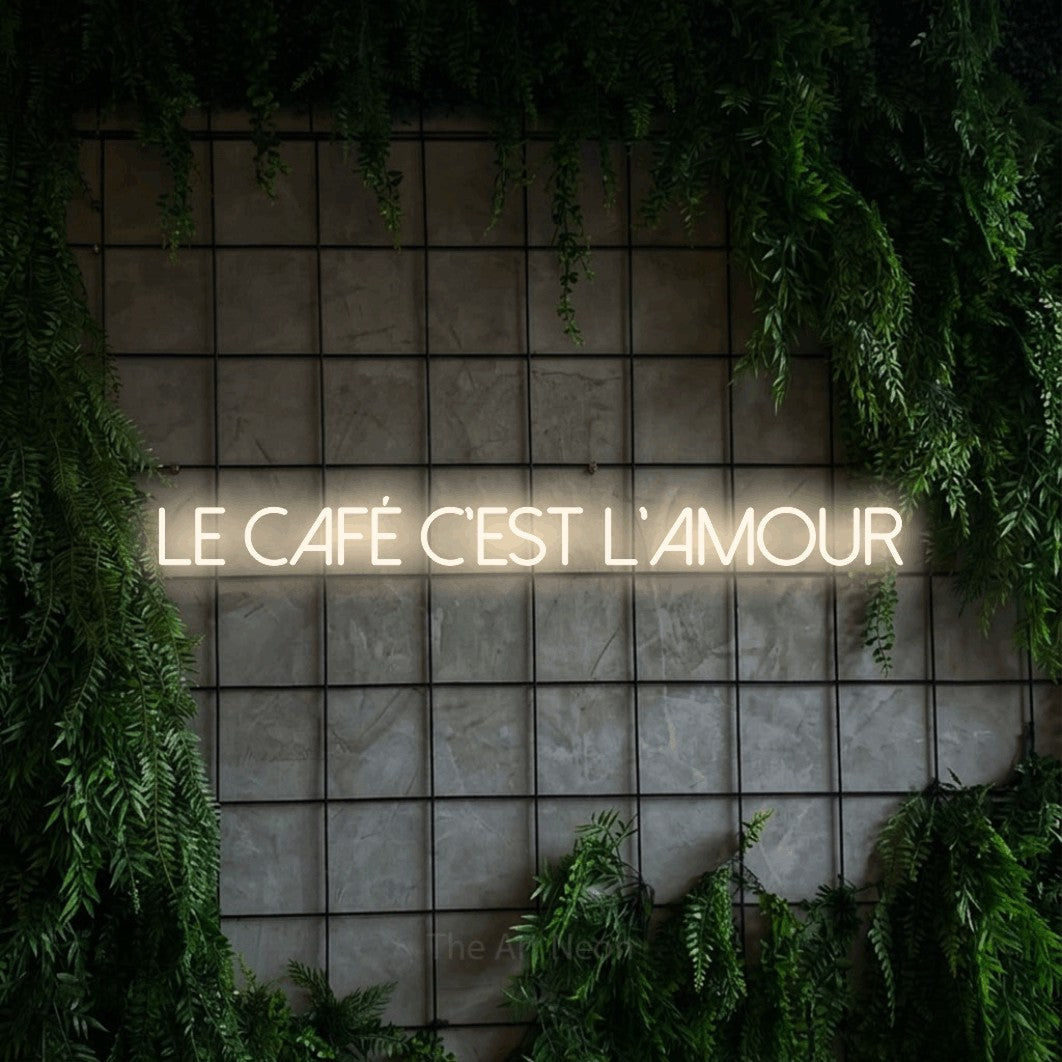 Aperçu d’une enseigne néon LED « Le café c'est l'amour » en blanc chaud, en lettres fines sans empattement, photographiée sur une grille de béton couverte de lierre, pour un café.