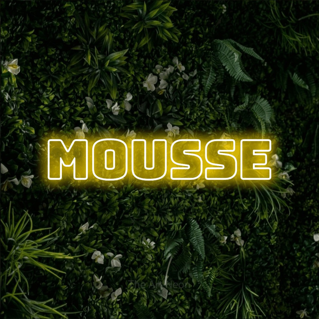 “Mousse” LED neon sign in yellow, with bold outline lettering, shown against a dense green plant wall.