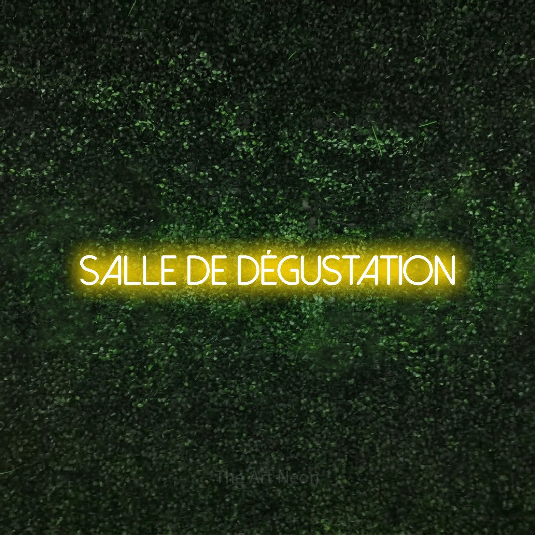 “Salle de dégustation” LED neon sign in yellow, with thin sans-serif lettering, shown against a textured green hedge.