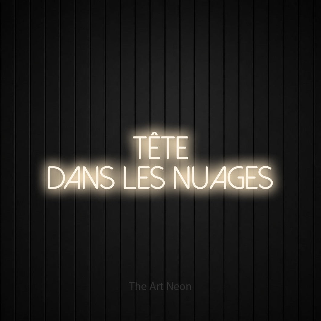 “Tête dans les nuages” LED neon sign in warm white, with thin sans-serif lettering across 2 lines, shown against black vertical wall slats.