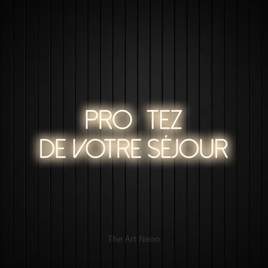 Lettrage en néon LED « Profitez de votre séjour » sur deux lignes en blanc chaud, en lettres fines sans empattement, présenté sur un mur de lattes verticales noires, pour un hôtel.