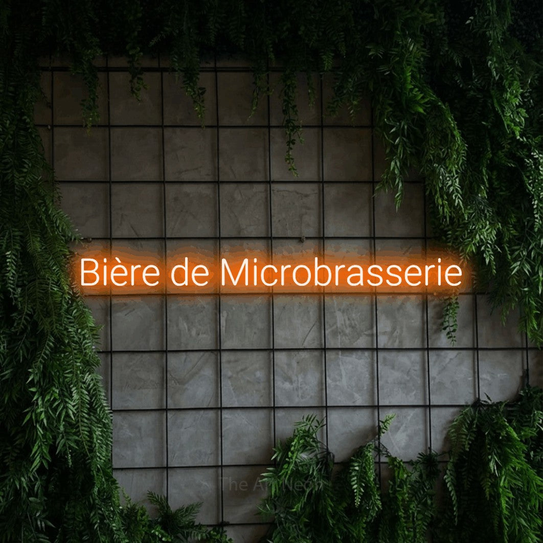 “Bière de microbrasserie” LED neon sign in orange, with rounded sans-serif lettering, shown against an ivy-covered concrete grid.