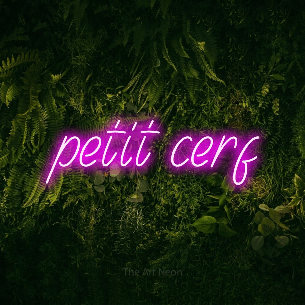 “Petit cerf” LED neon sign in pink, with slanted handwritten lettering, shown against a dark moss and forest backdrop.