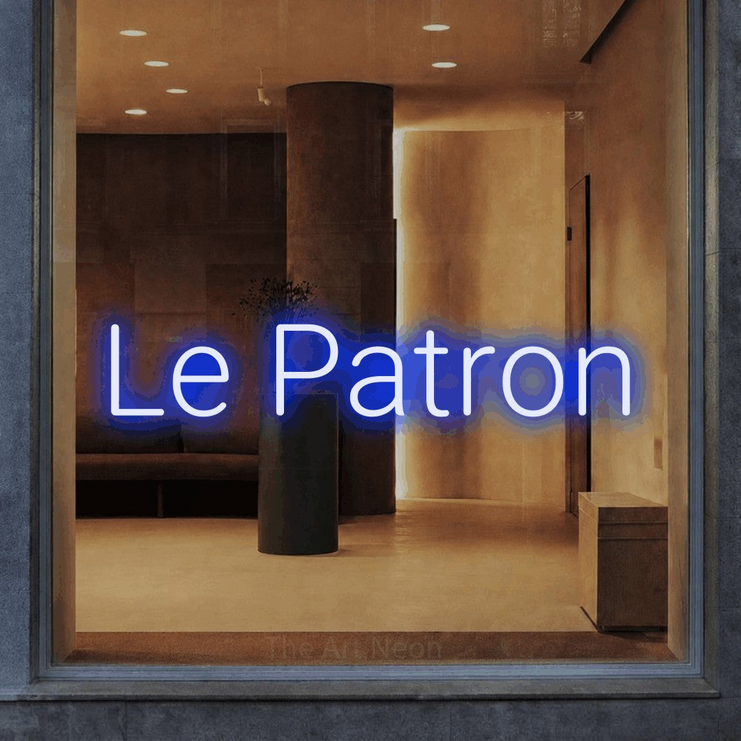 “Le patron” LED neon sign in blue, with rounded sans-serif lettering, shown against a warm-toned interior.