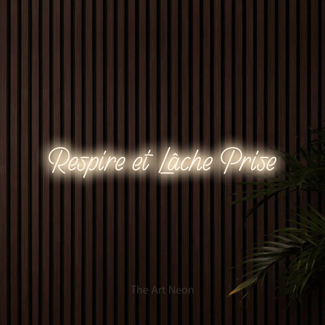 Composition en néon LED « Respire et lâche prise » en blanc chaud, en écriture manuscrite inclinée, mise en valeur sur un mur de lattes en bois foncé, pour un espace d’entraînement.