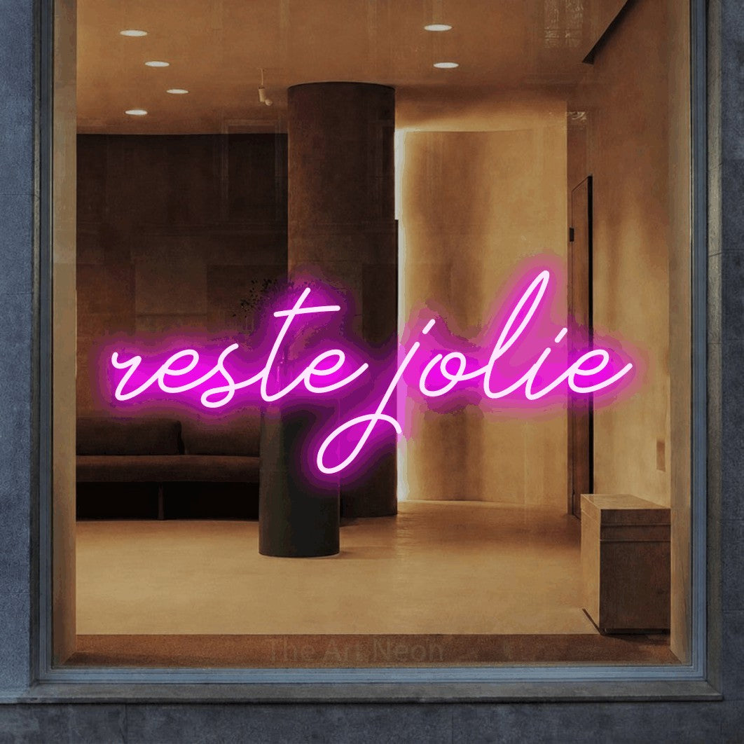 “Reste jolie” LED neon sign in pink, with cursive lettering, shown against a warm-toned interior.