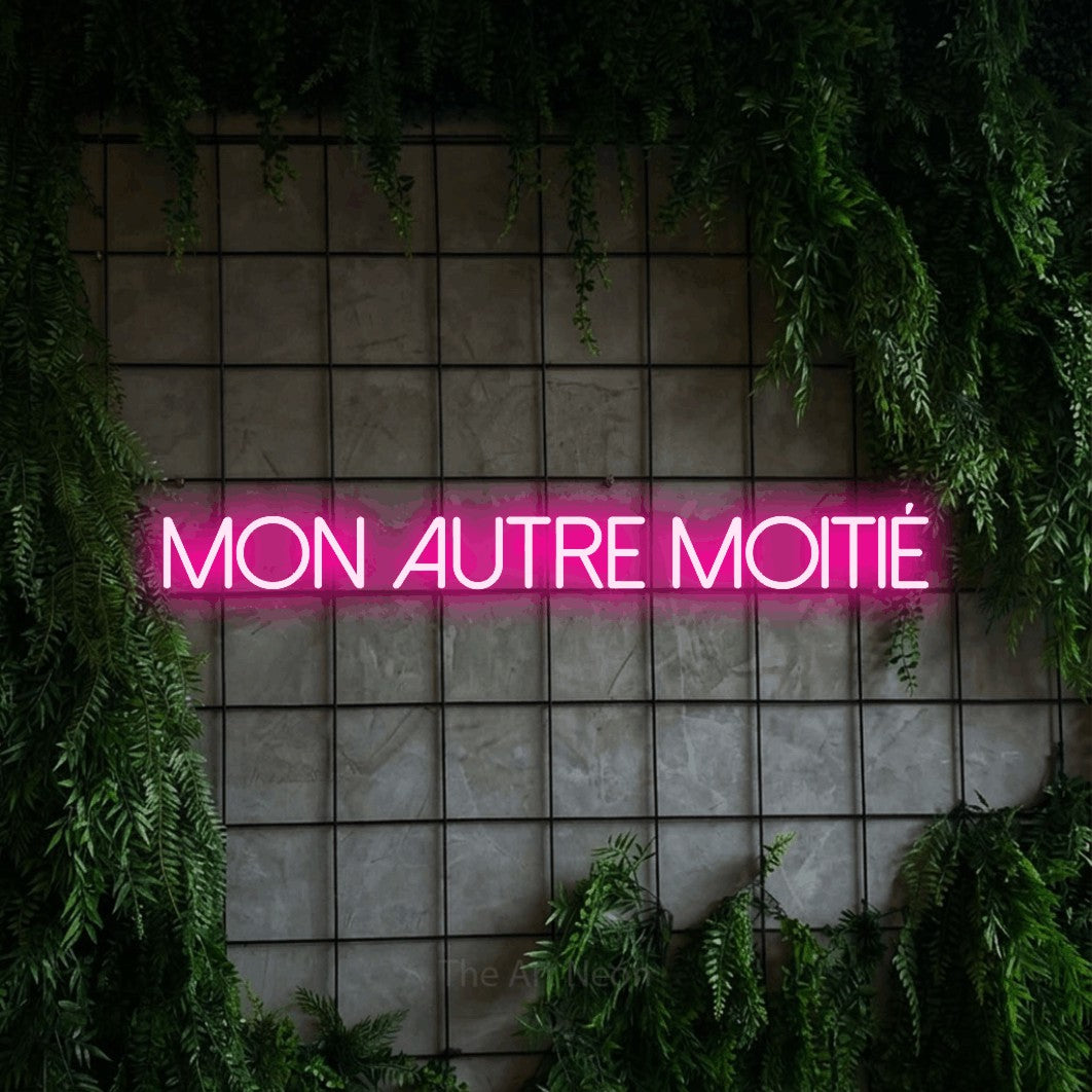 “Mon autre moitié” LED neon sign in hot pink, with thin sans-serif lettering, shown against an ivy-covered concrete grid.