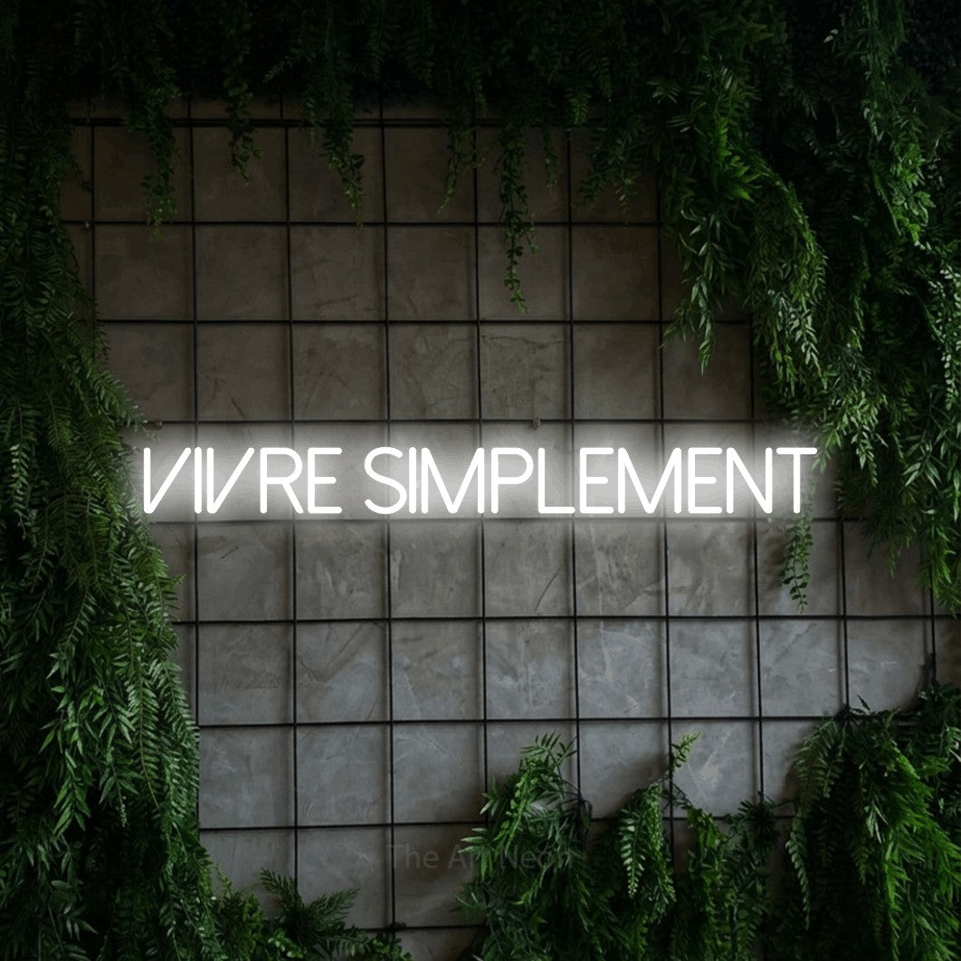 “Vivre simplement” LED neon sign in cool white, with thin sans-serif lettering, shown against an ivy-covered concrete grid.