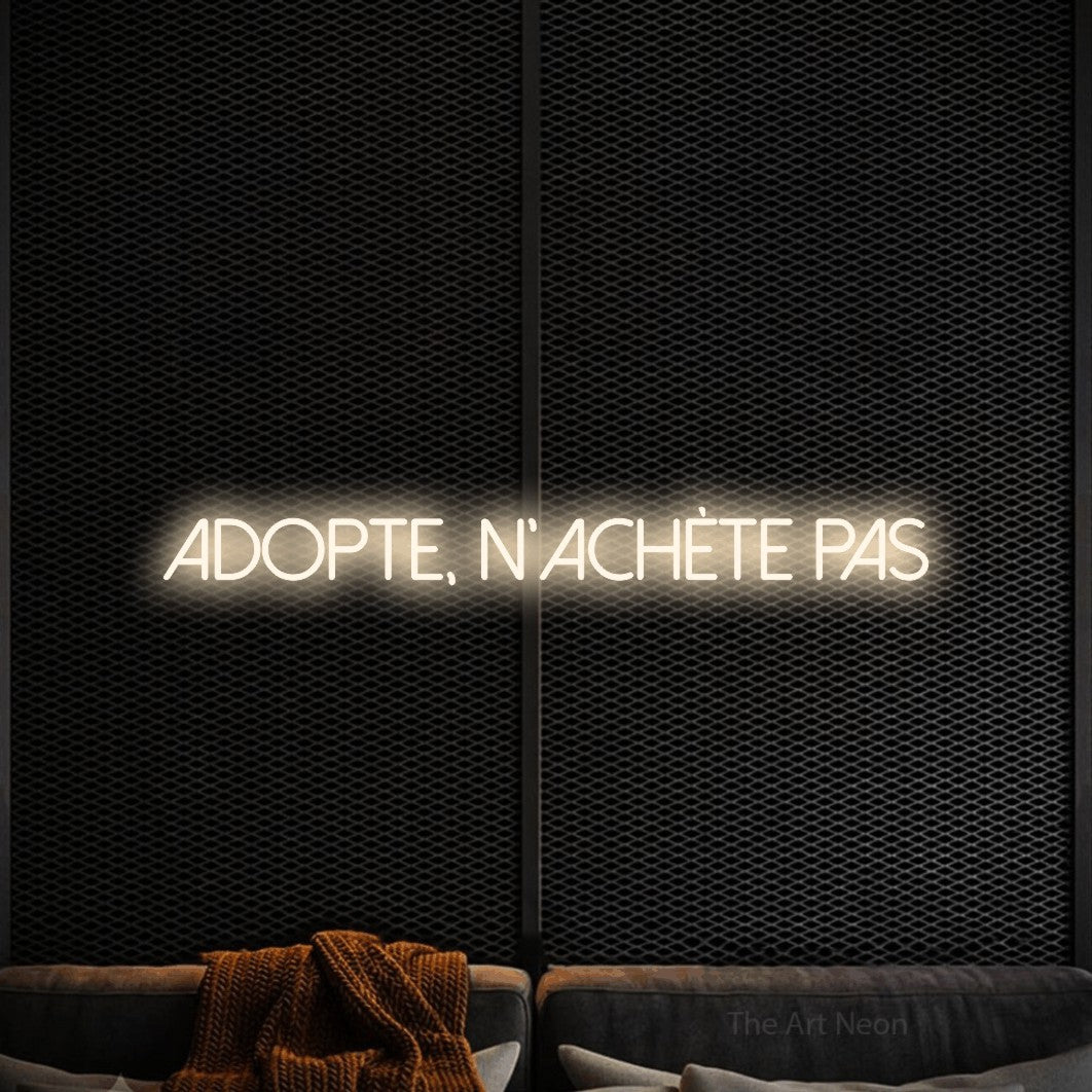 “Adopte, n'achète pas” LED neon sign in warm white, with thin sans-serif lettering, shown against a modern dark-toned seating area.