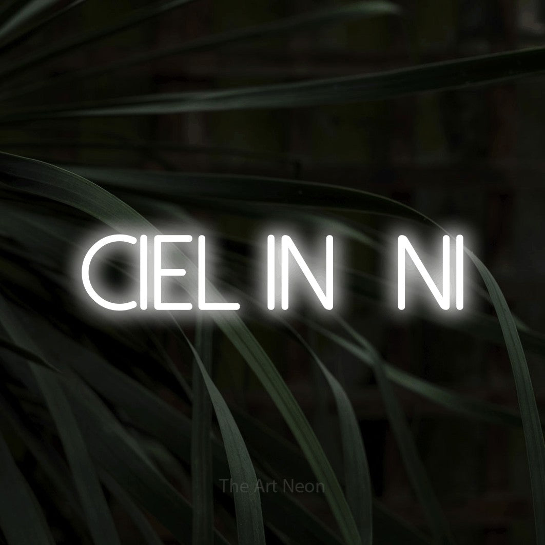 “Ciel infini” LED neon sign in cool white, with thin sans-serif lettering, shown against a close-up of dark foliage.