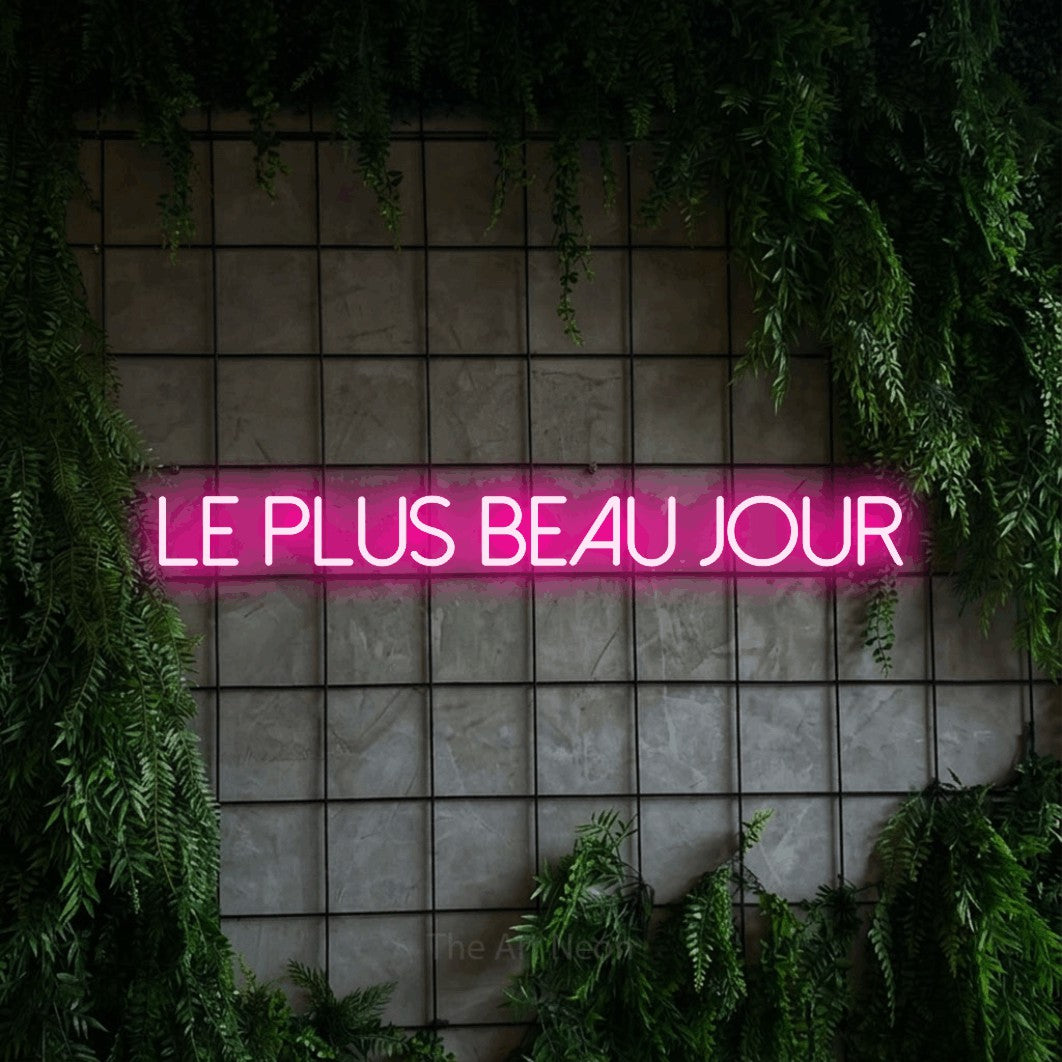 “Le plus beau jour” LED neon sign in hot pink, with thin sans-serif lettering, shown against an ivy-covered concrete grid.