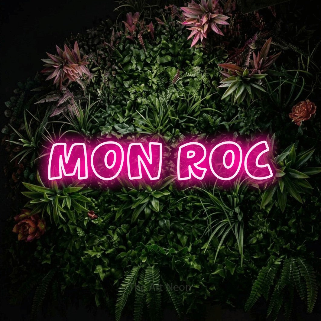 “Mon roc” LED neon sign in hot pink, with rounded outline lettering, shown against a flowering plant wall.