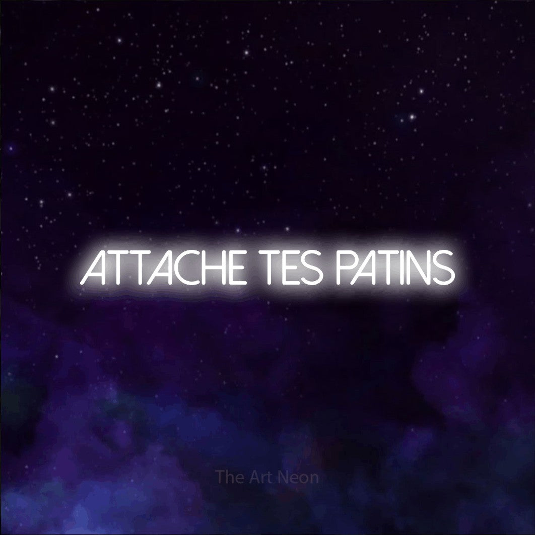 “Attache tes patins” LED neon sign in cool white, with thin sans-serif lettering, shown against a purple galaxy backdrop.