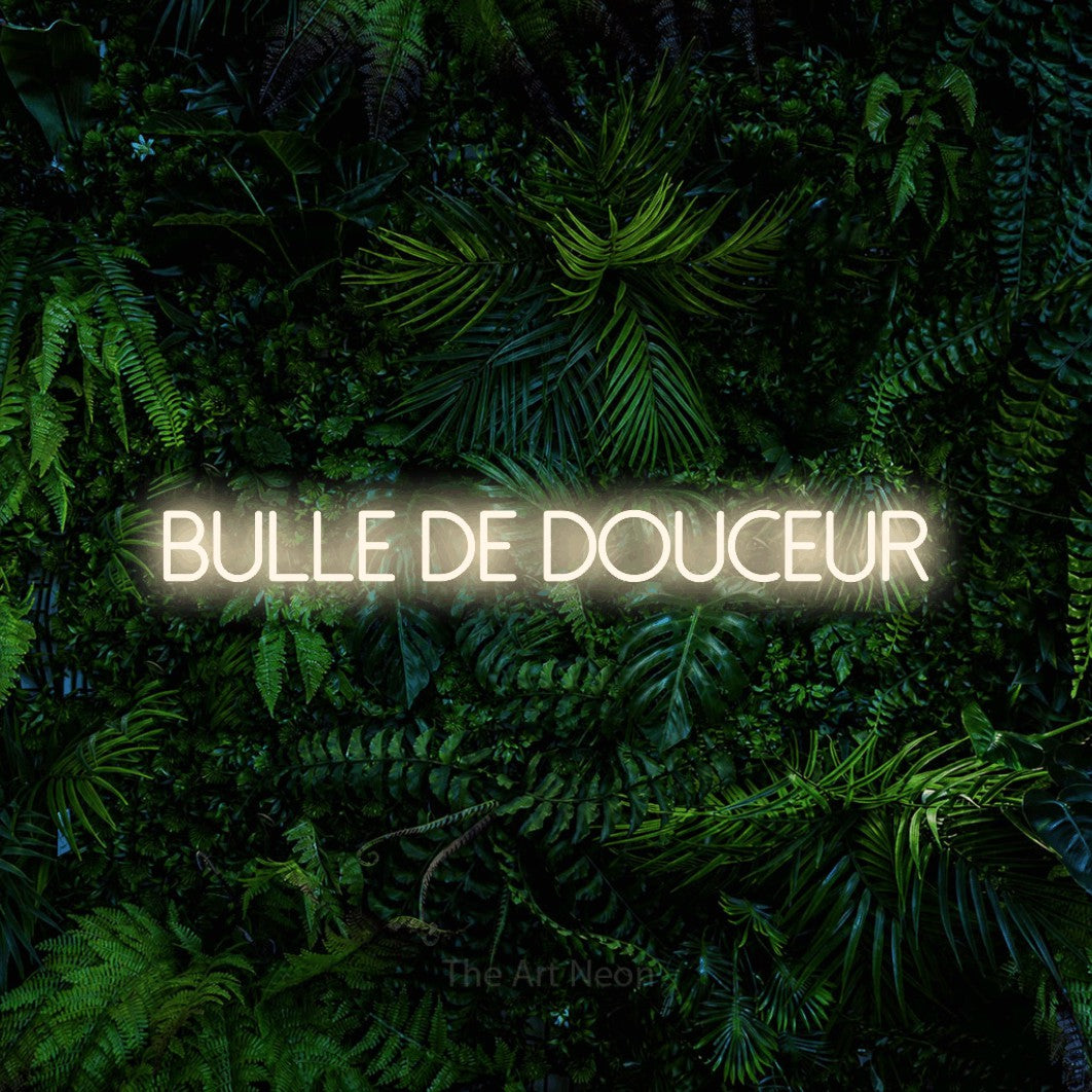 “Bulle de douceur” LED neon sign in warm white, with thin sans-serif lettering, shown against dense tropical foliage.