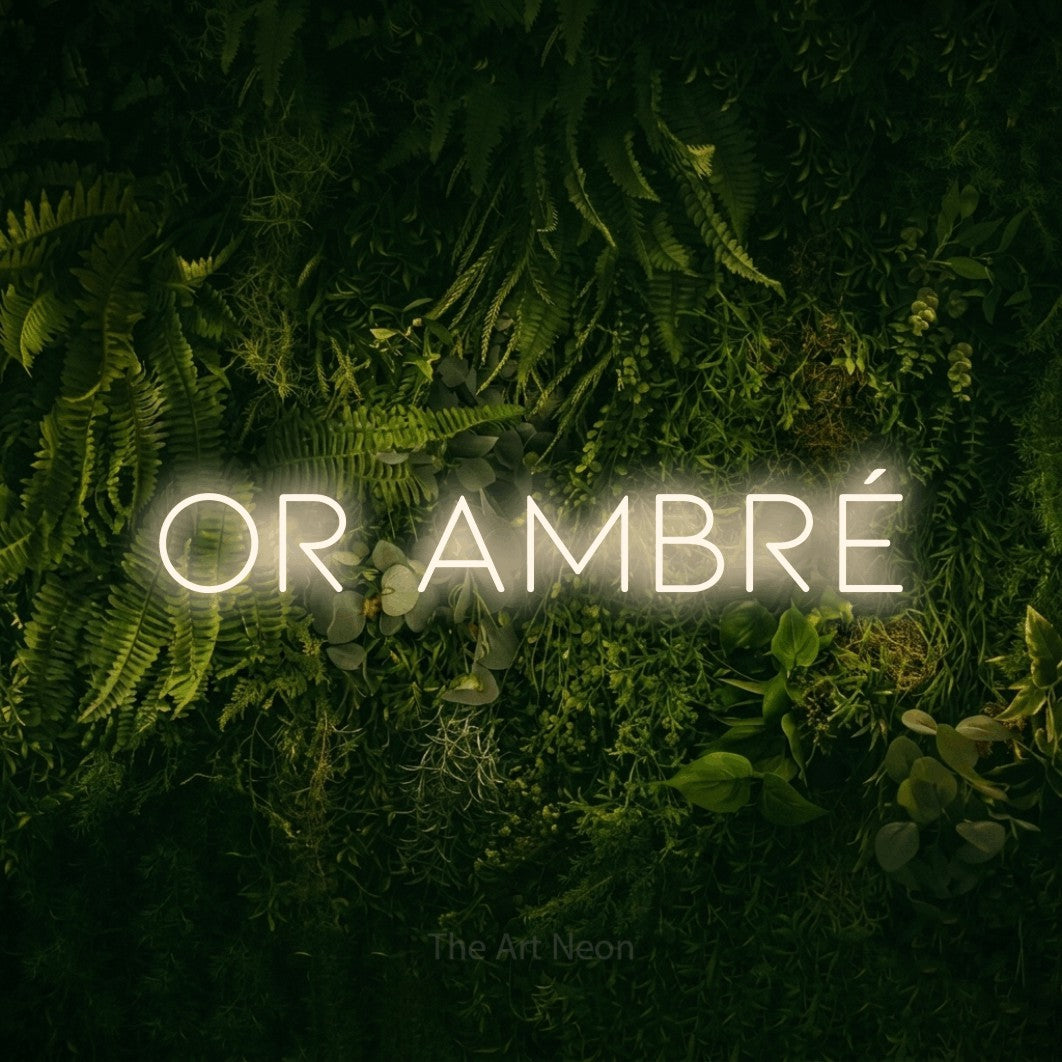 “Or ambré” LED neon sign in warm white, with thin, widely spaced lettering, shown against a dark moss and forest backdrop.