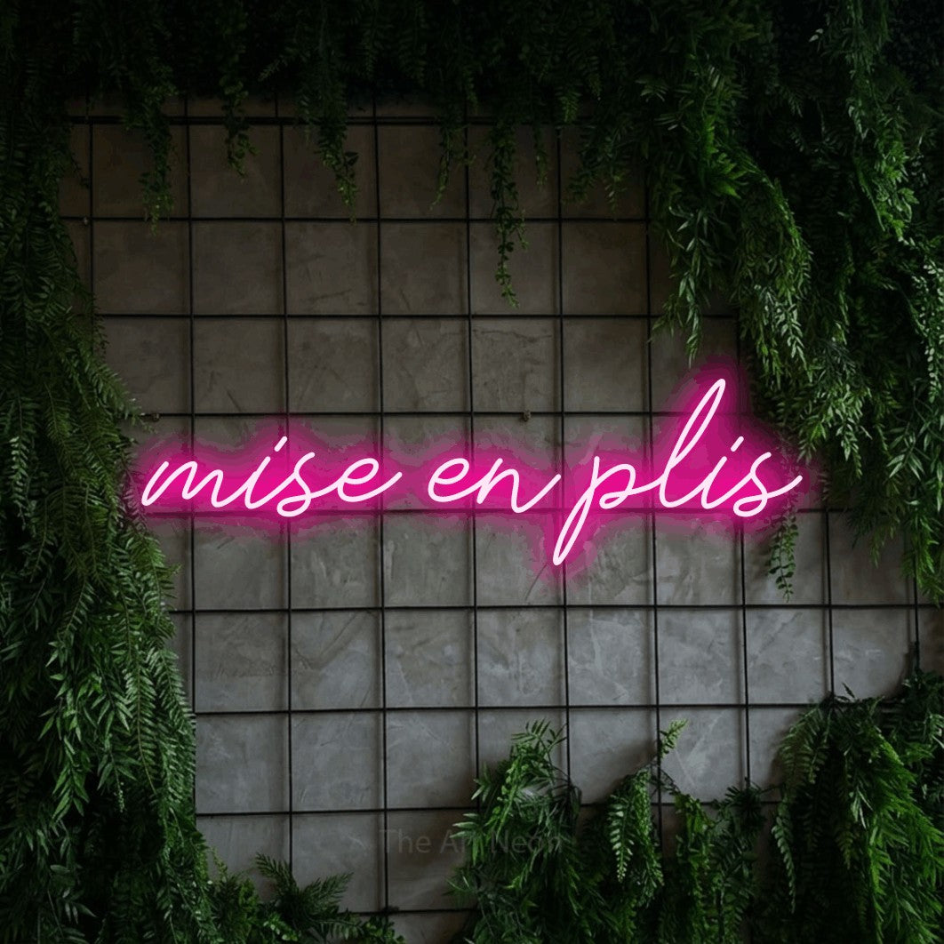 “Mise en plis” LED neon sign in hot pink, with cursive lettering, shown against an ivy-covered concrete grid.