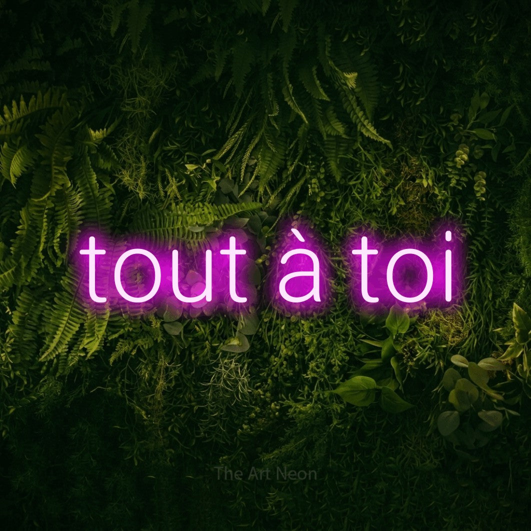 “Tout à toi” LED neon sign in pink, with rounded sans-serif lettering, shown against a dark moss and forest backdrop.