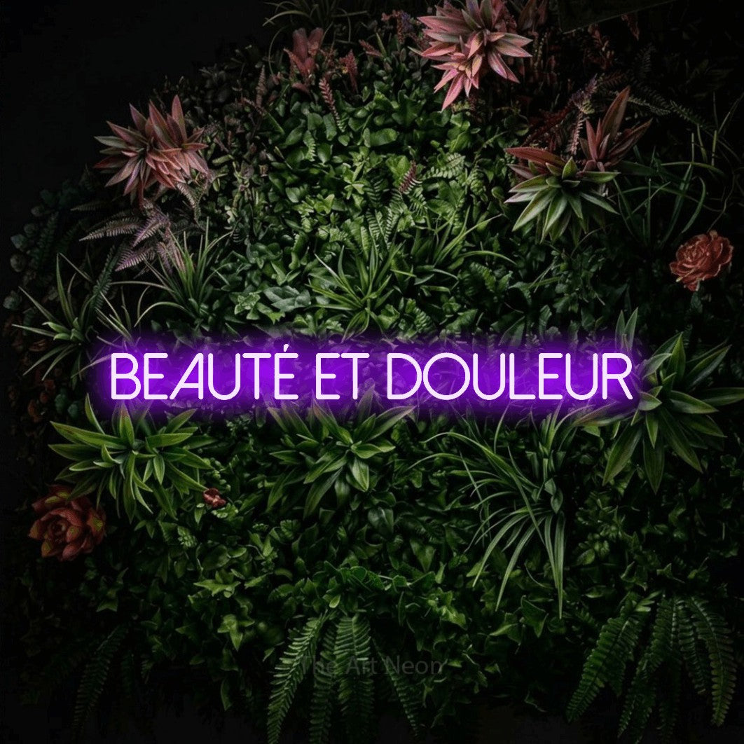 “Beauté et douleur” LED neon sign in purple, with thin sans-serif lettering, shown against a flowering plant wall.