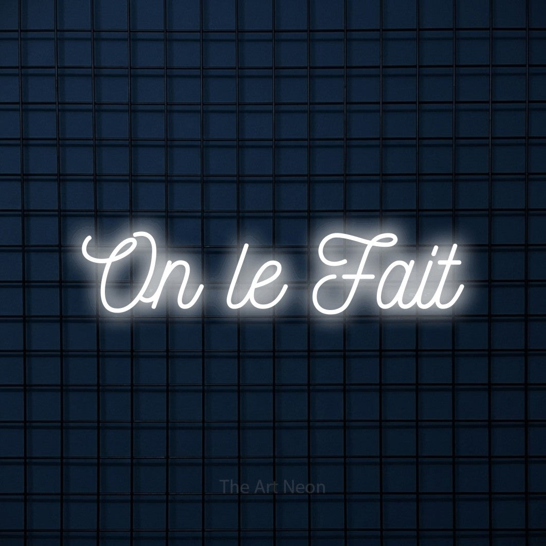 “On le fait” LED neon sign in cool white, with ornate cursive lettering, shown against a dark blue grid.