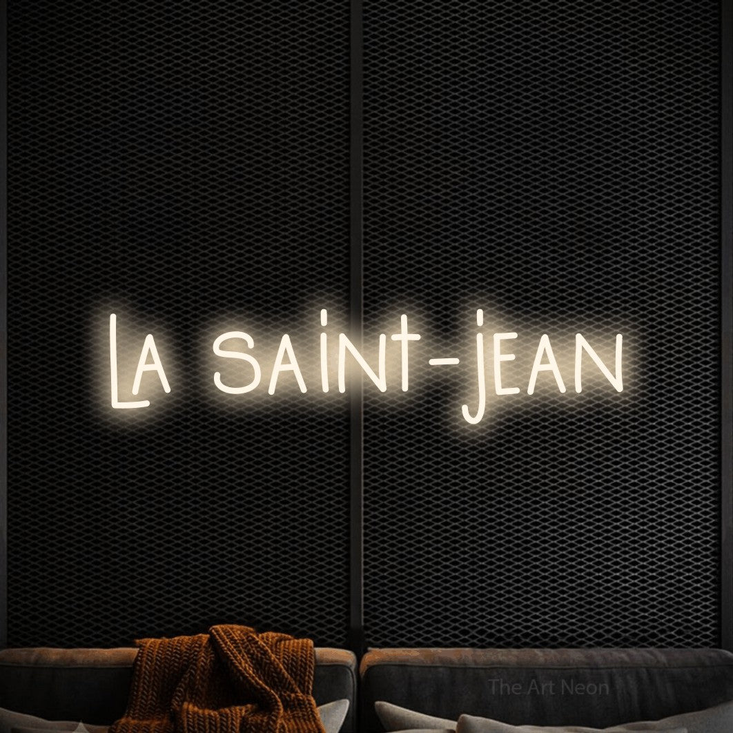 “La Saint-Jean” LED neon sign in warm white, with narrow hand-drawn lettering, shown against a modern dark-toned seating area.
