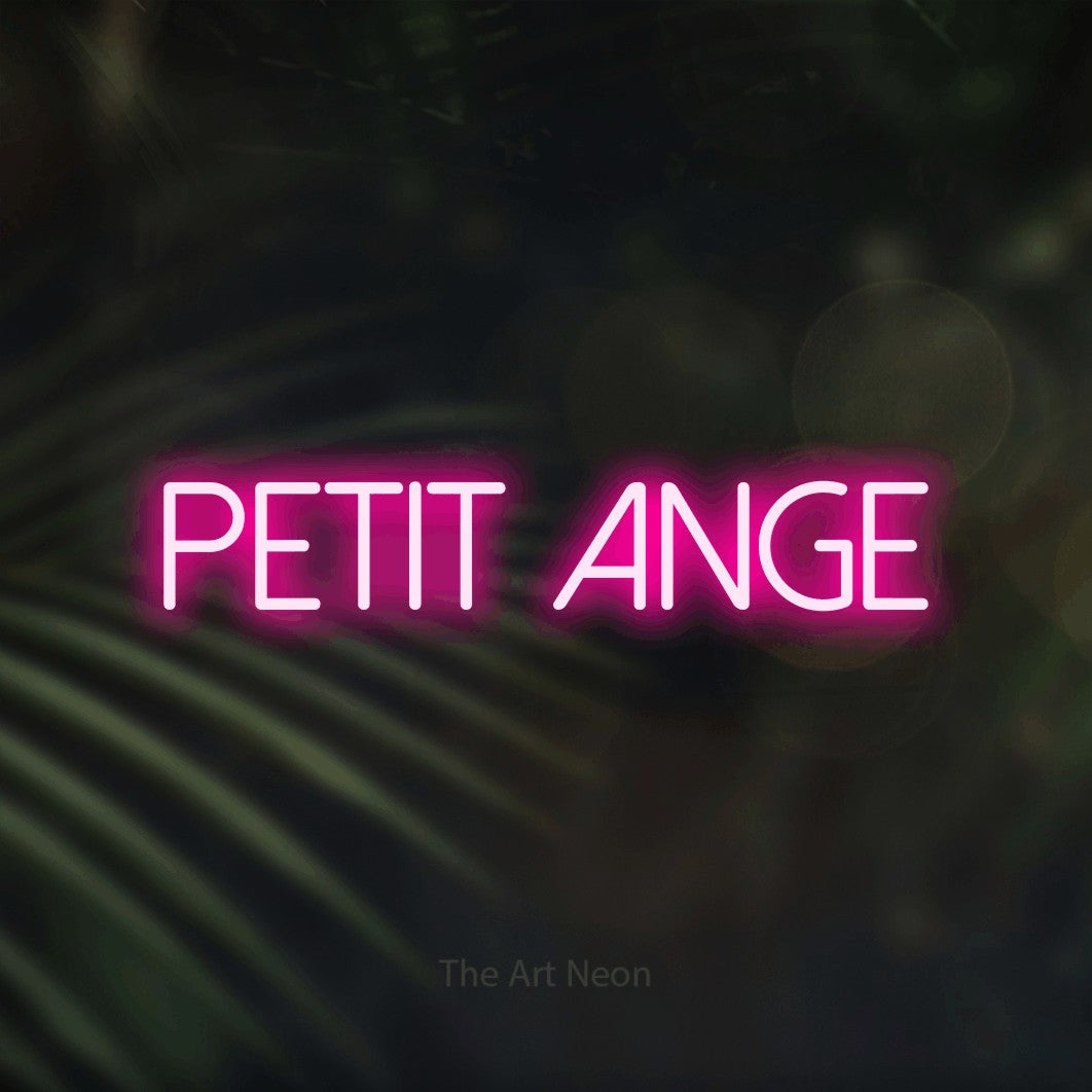 “Petit ange” LED neon sign in hot pink, with thin sans-serif lettering, shown against a blurred palm and bokeh-light backdrop.