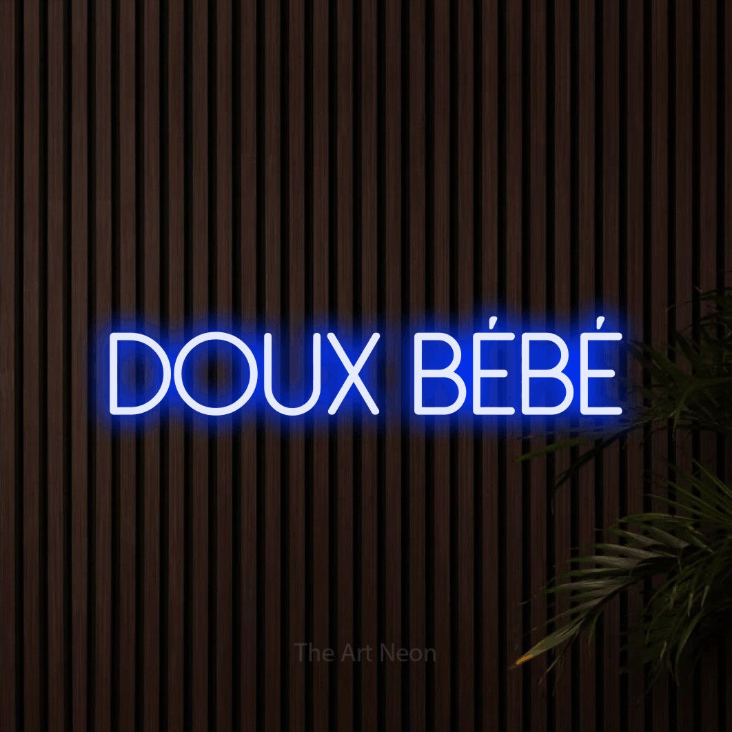 “Doux bébé” LED neon sign in blue, with thin sans-serif lettering, shown against dark wooden wall slats.
