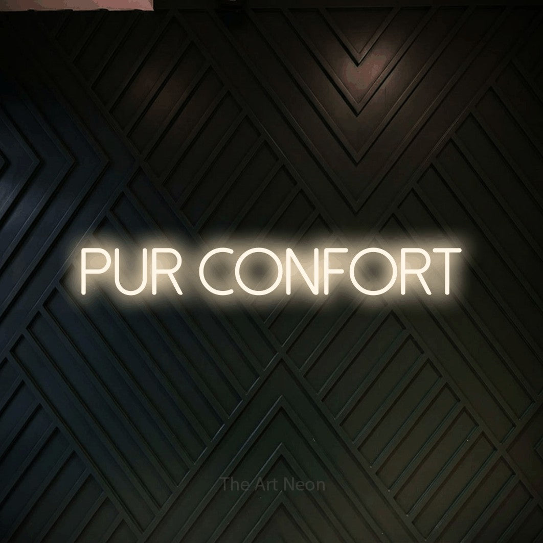 “Pur confort” LED neon sign in warm white, with thin sans-serif lettering, shown against a black chevron-patterned wood wall.