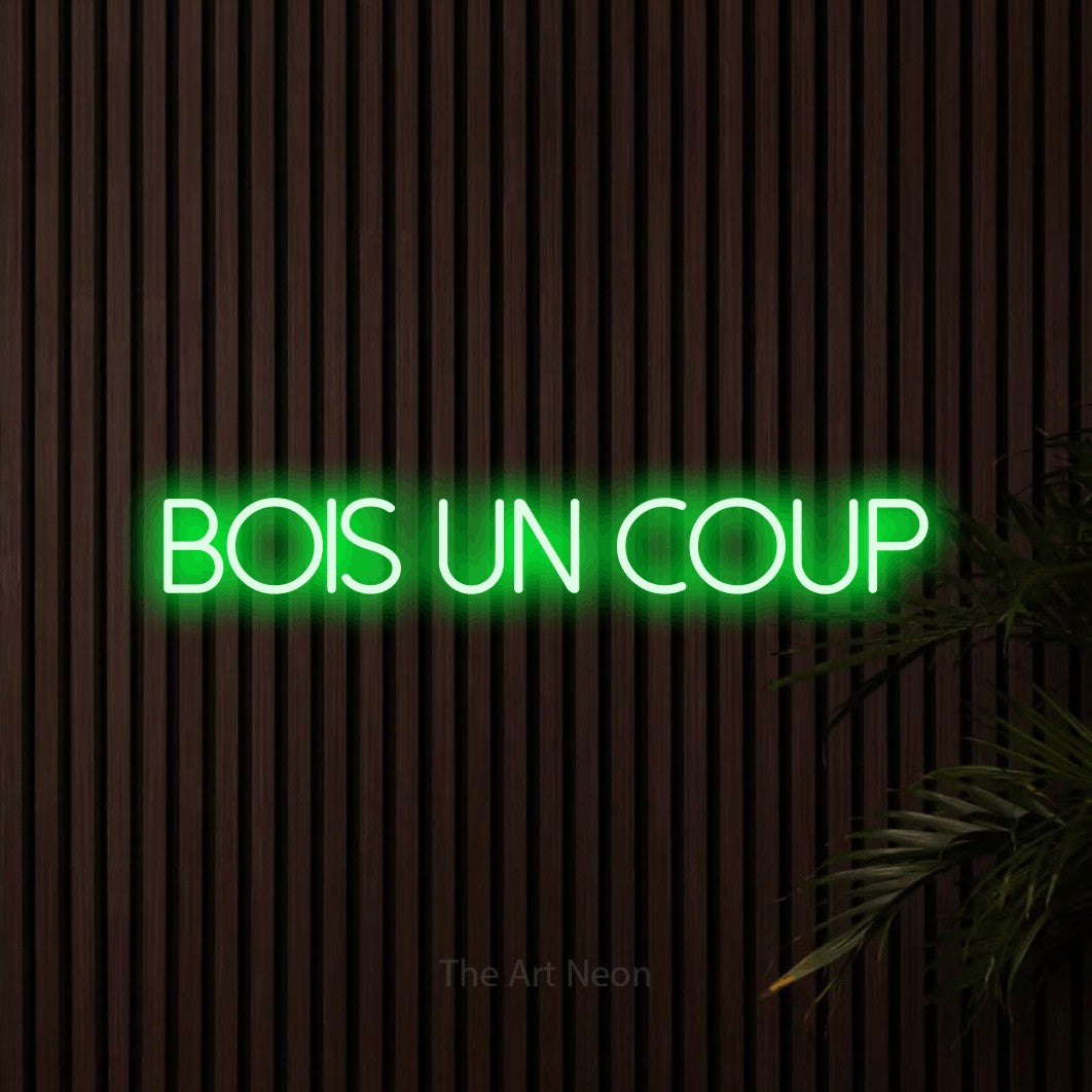“Bois un coup” LED neon sign in green, with thin sans-serif lettering, shown against dark wooden wall slats.