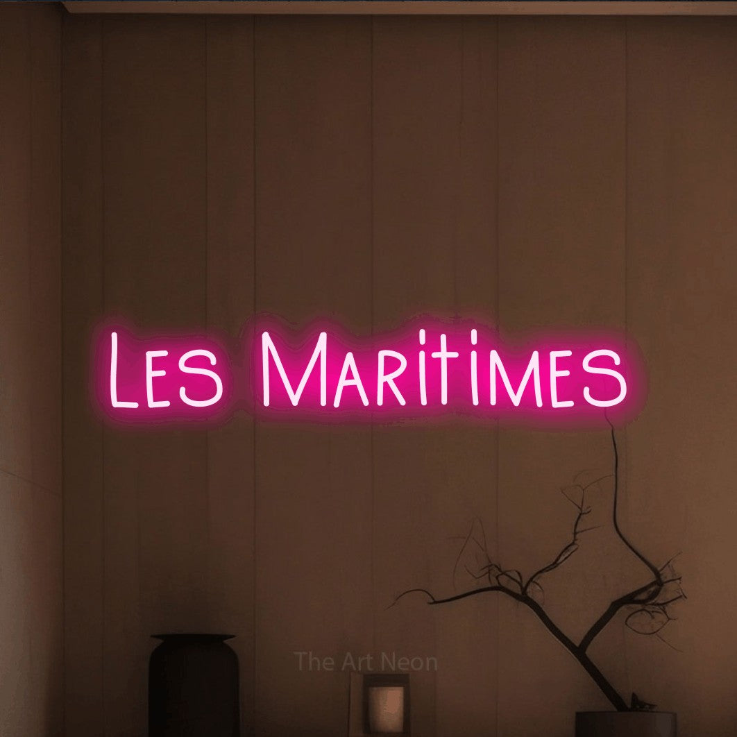 “Les maritimes” LED neon sign in hot pink, with narrow hand-drawn lettering, shown against a simple earth-toned interior.