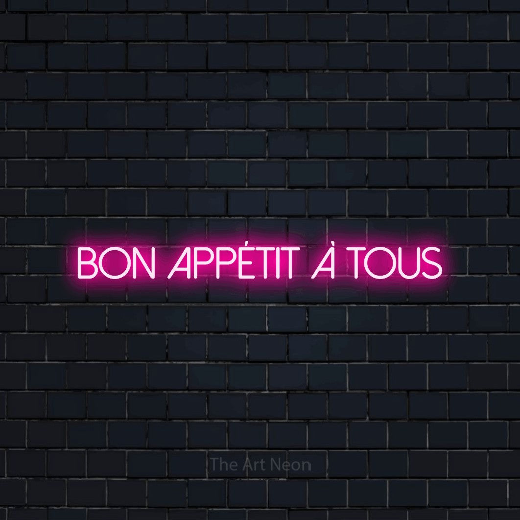 “Bon appétit à tous” LED neon sign in hot pink, with thin sans-serif lettering, shown against a dark navy brick wall.