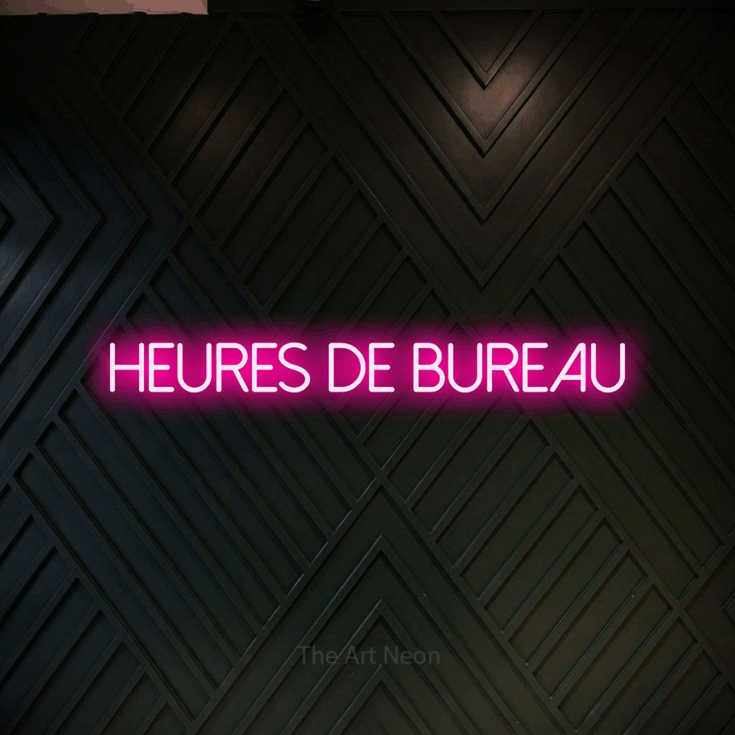 “Heures de bureau” LED neon sign in hot pink, with thin sans-serif lettering, shown against a black chevron-patterned wood wall.