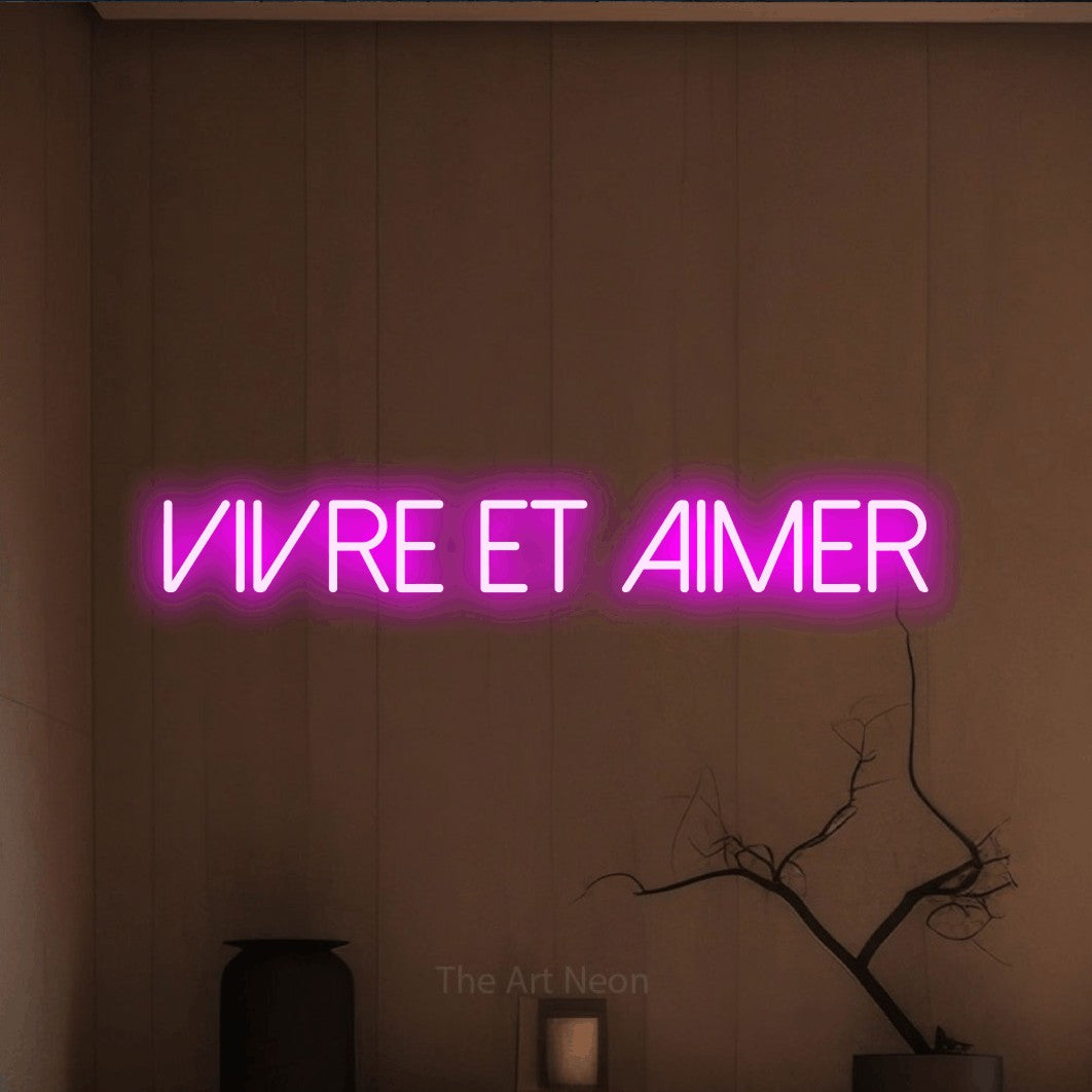“Vivre et aimer” LED neon sign in pink, with thin sans-serif lettering, shown against a simple earth-toned interior.