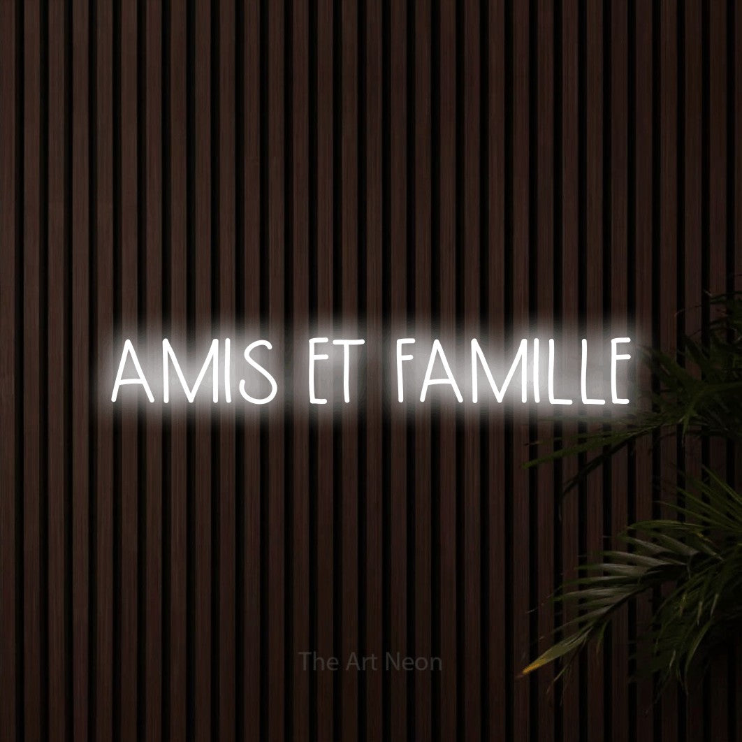 Lettrage en néon LED « Amis et famille » en blanc froid, en lettres étroites dessinées à la main, présenté sur un mur de lattes en bois foncé, pour un salon.