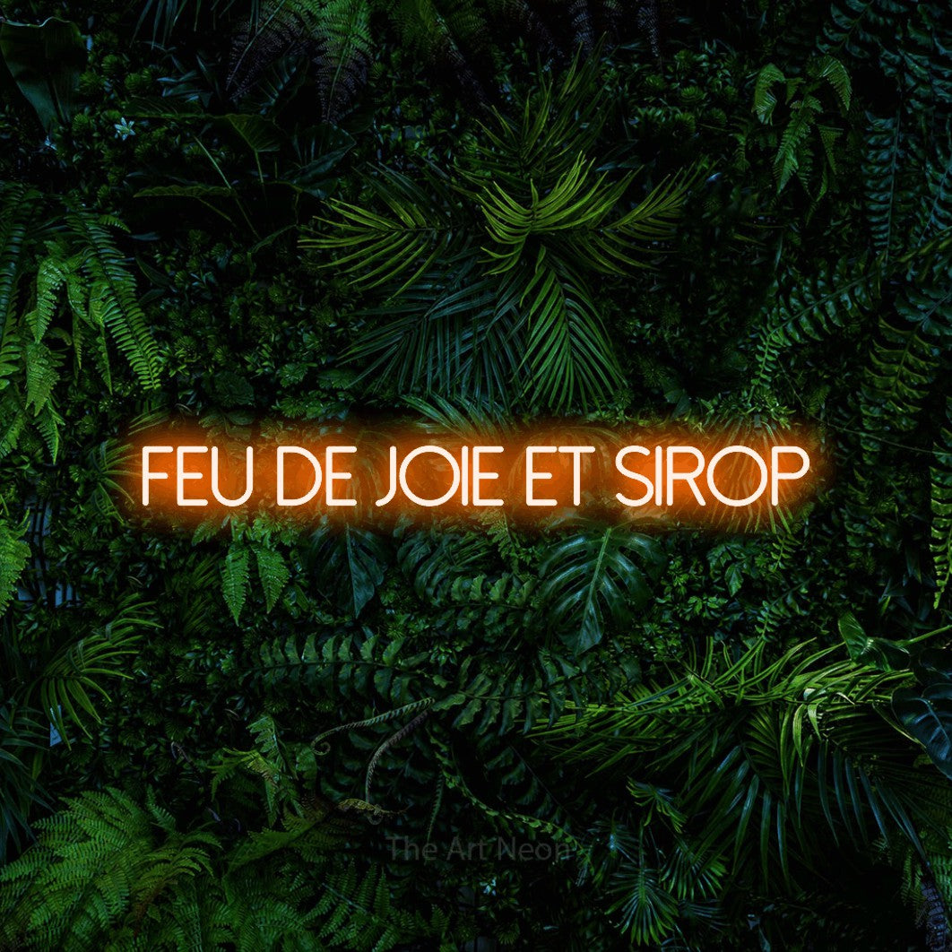 “Feu de joie et sirop” LED neon sign in orange, with thin sans-serif lettering, shown against dense tropical foliage.