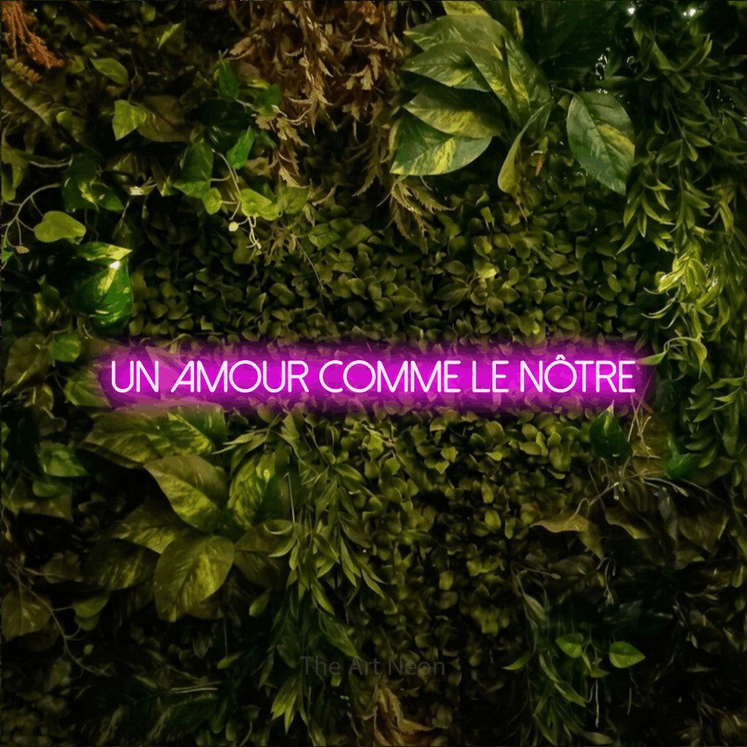 “Un amour comme le nôtre” LED neon sign in pink, with thin sans-serif lettering, shown against bright green and yellow foliage.