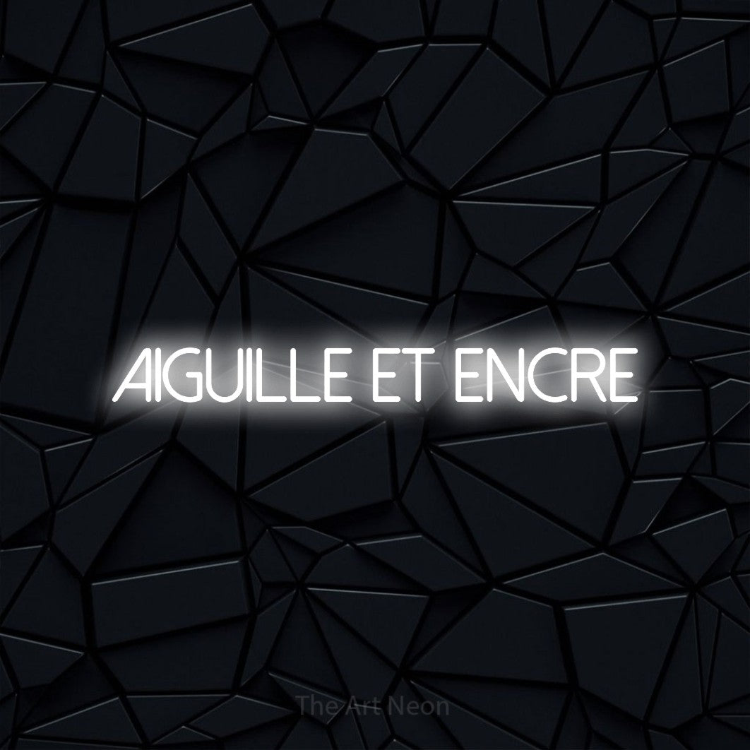 “Aiguille et encre” LED neon sign in cool white, with thin sans-serif lettering, shown against a black polygonal surface.