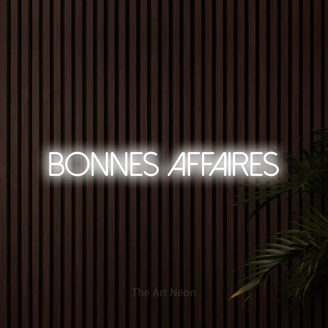 “Bonnes affaires” LED neon sign in cool white, with thin sans-serif lettering, shown against dark wooden wall slats.