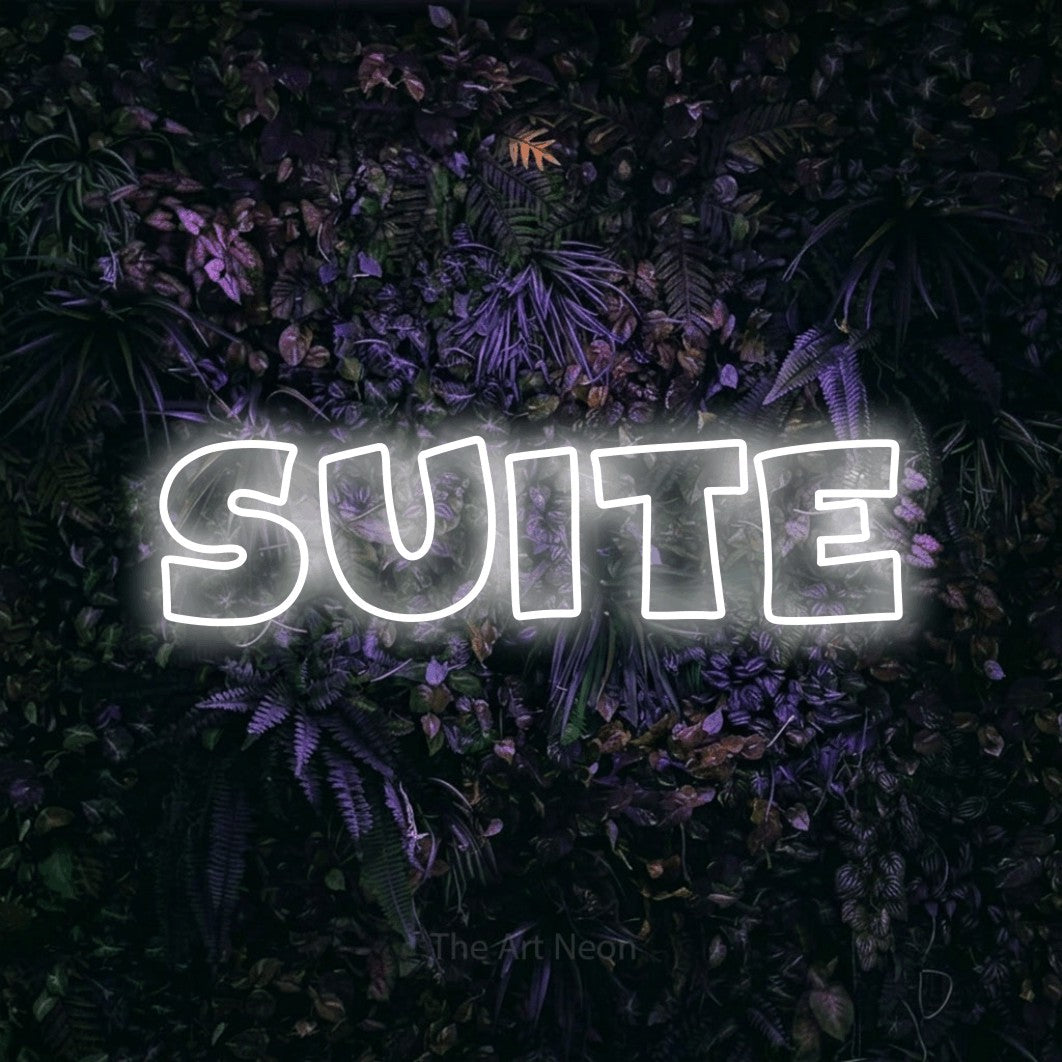 “Suite” LED neon sign in cool white, with wide lettering with irregular outlines, shown against a dark wall with purple flowers.