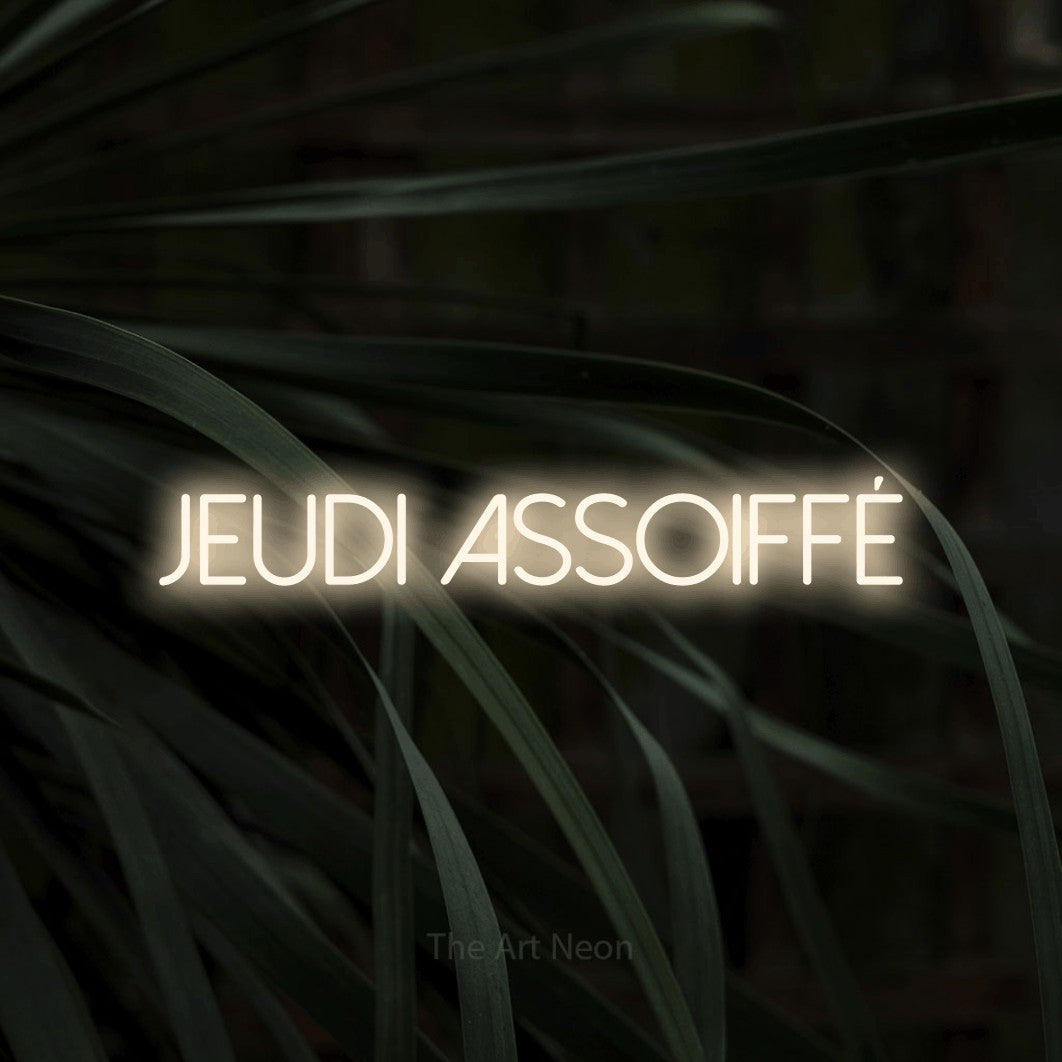 Aperçu d’une enseigne néon LED « Jeudi assoiffé » en blanc chaud, en lettres fines sans empattement, photographiée sur un feuillage sombre en gros plan, pour un bar ou un pub.