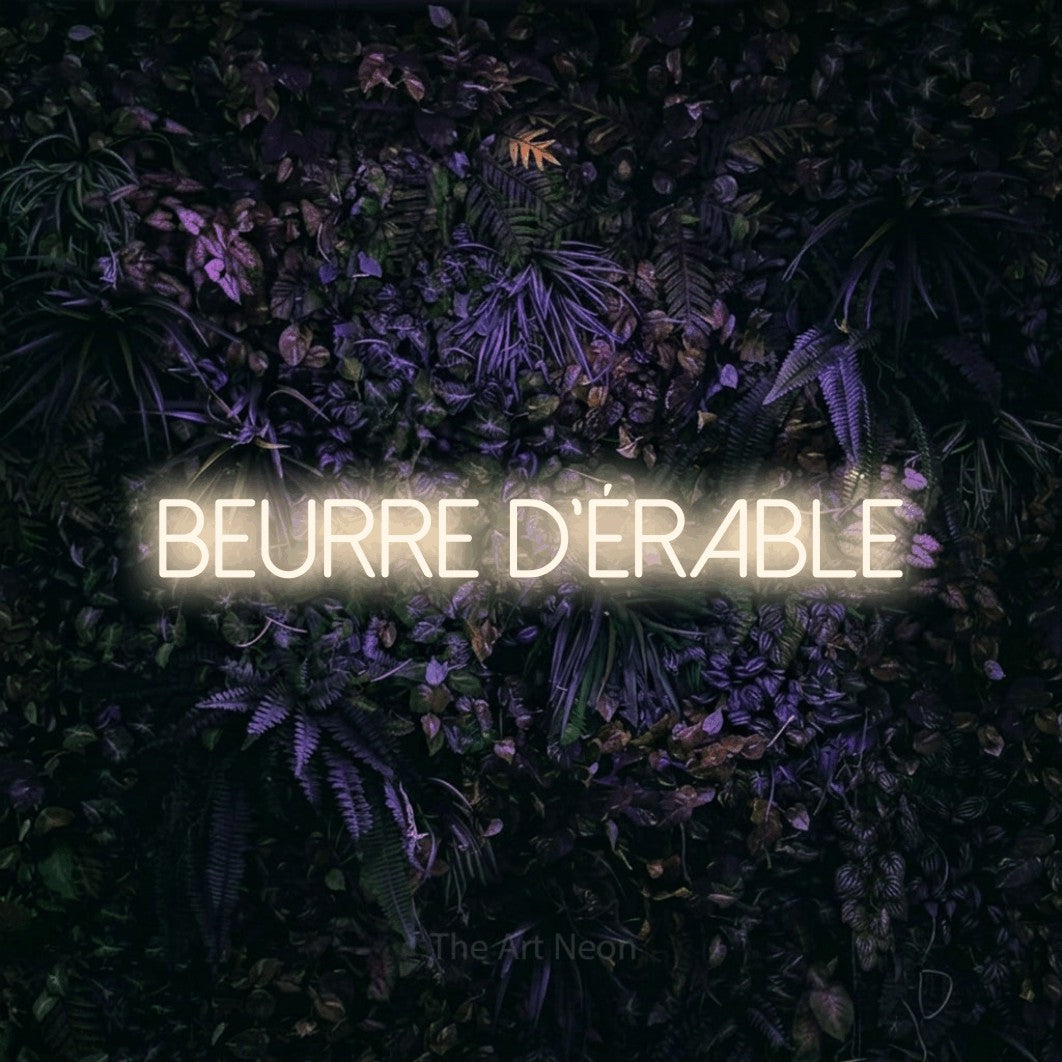 “Beurre d'érable” LED neon sign in warm white, with thin sans-serif lettering, shown against a dark wall with purple flowers.