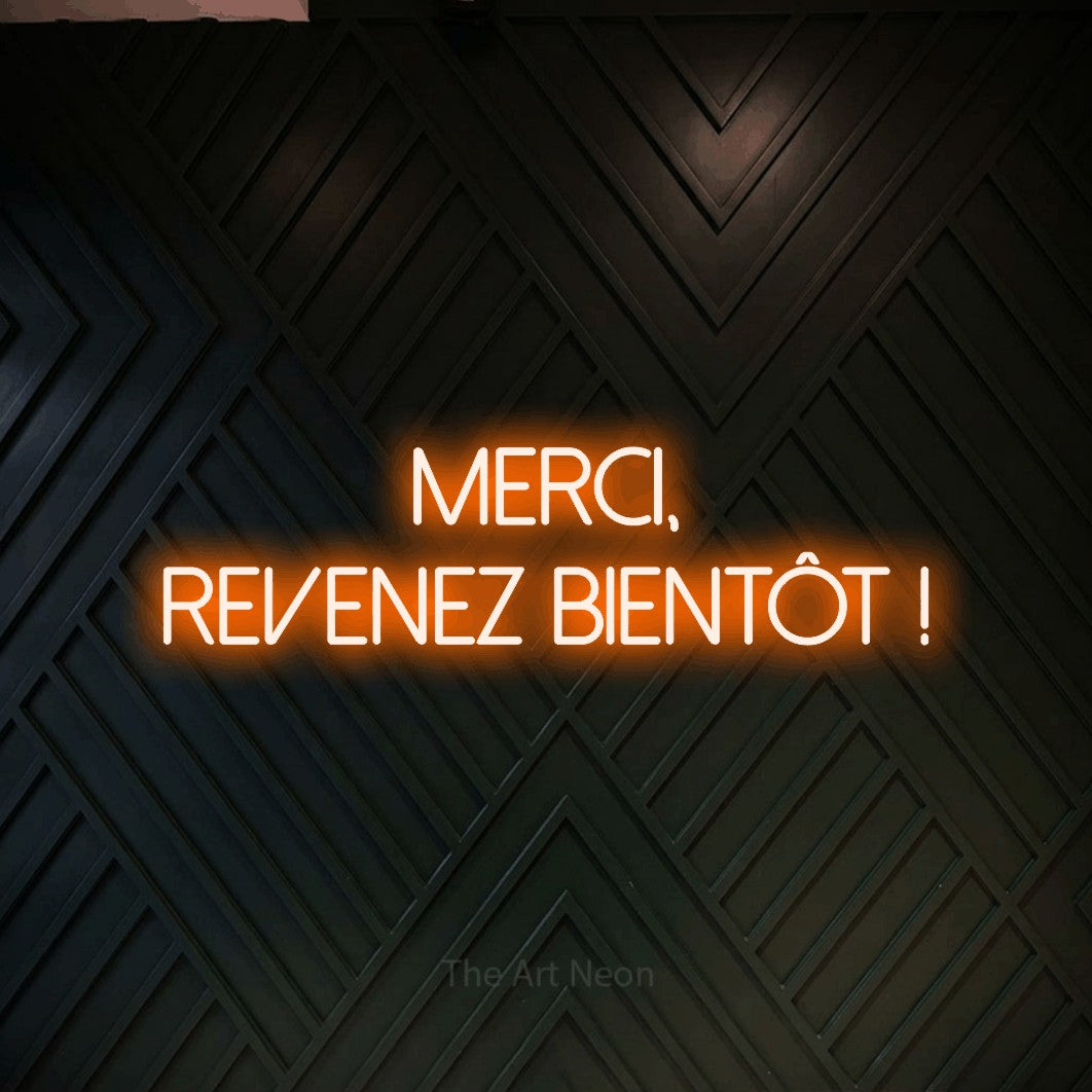 “Merci, revenez bientôt !” LED neon sign in orange, with thin sans-serif lettering across 2 lines, shown against a black chevron-patterned wood wall.