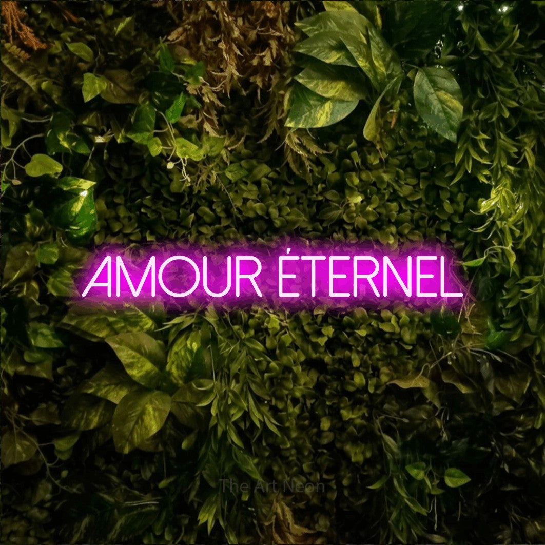 “Amour éternel” LED neon sign in pink, with thin sans-serif lettering, shown against bright green and yellow foliage.