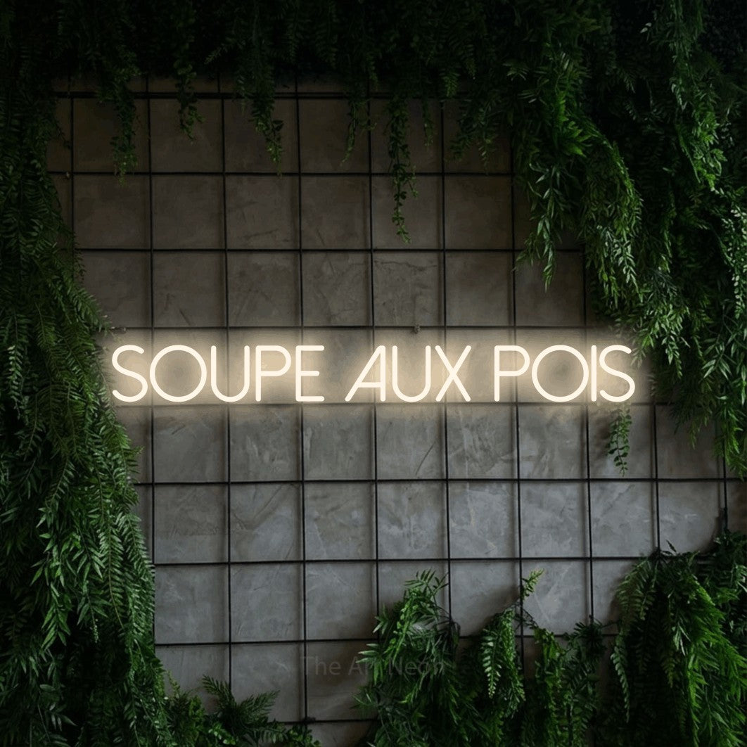 “Soupe aux pois” LED neon sign in warm white, with thin sans-serif lettering, shown against an ivy-covered concrete grid.